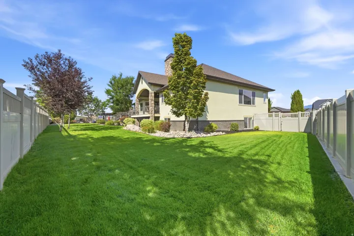 Expansive backyard featuring a lush lawn, privacy fencing, mature trees, and a stone-clad chimney