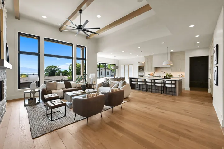 Vaulted ceilings with exposed beams, wood-finish flooring, a stone-clad fireplace, and large-format windows