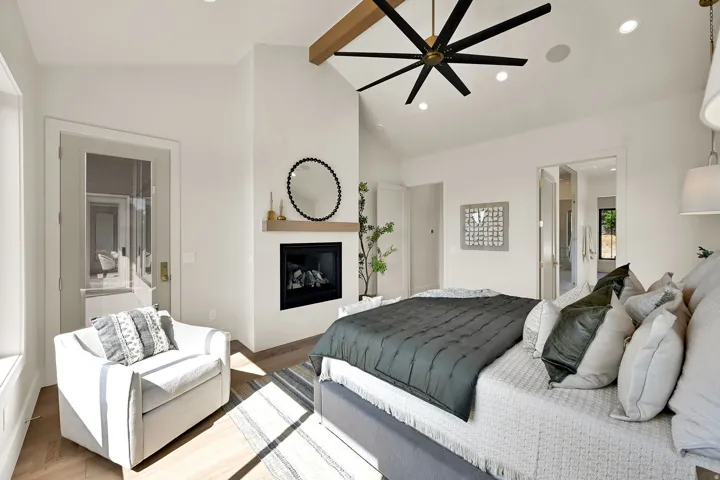 Vaulted ceiling with exposed wood beam, recessed lighting, ceiling fan, fireplace with wood mantel, and wood-finish flooring
