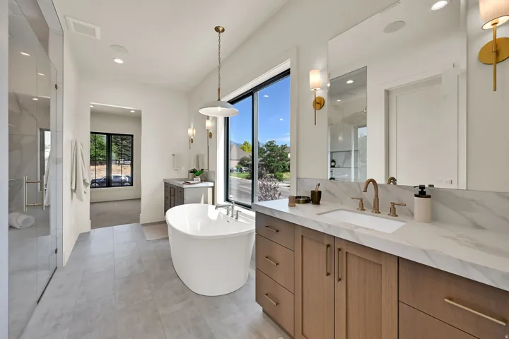 Freestanding soaking tub, dual vanity with undermount sink, built-in cabinetry, walk-in shower with glass enclosure, and large window