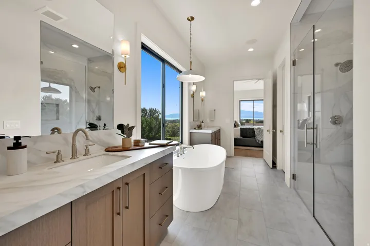 Spacious bathroom featuring a freestanding soaking tub, expansive window, glass-enclosed shower, dual vanity with undermount sink, and large format tile flooring