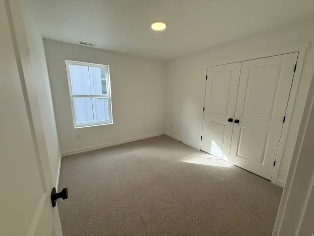 Neutral-toned carpet flooring, white walls, double-panel bifold closet doors with matte black hardware, and a single window with white trim