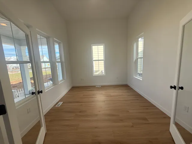 Vaulted ceiling, wood-finish flooring, white walls, multiple windows, and a glass-paneled entry door