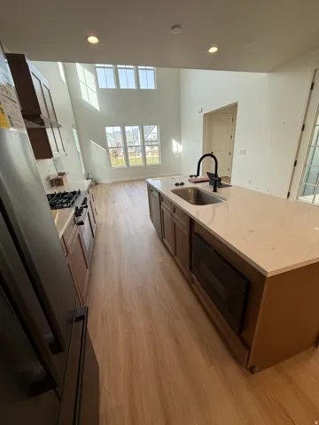 Two-story ceiling, recessed lighting, wood-finish flooring, central island with integrated sink, and upper and lower windows