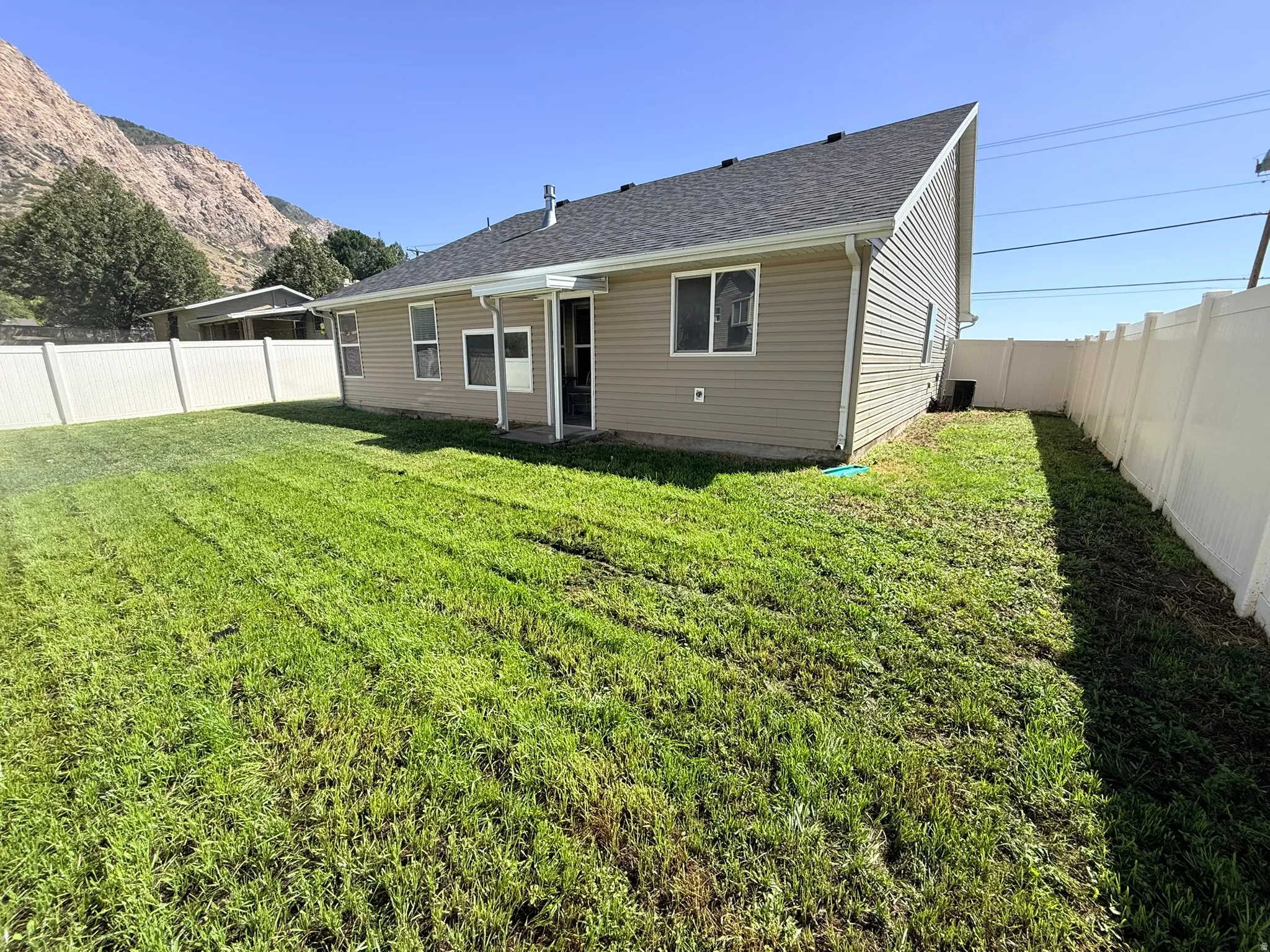 Expansive backyard featuring a manicured lawn, full vinyl privacy fencing, and a covered patio area