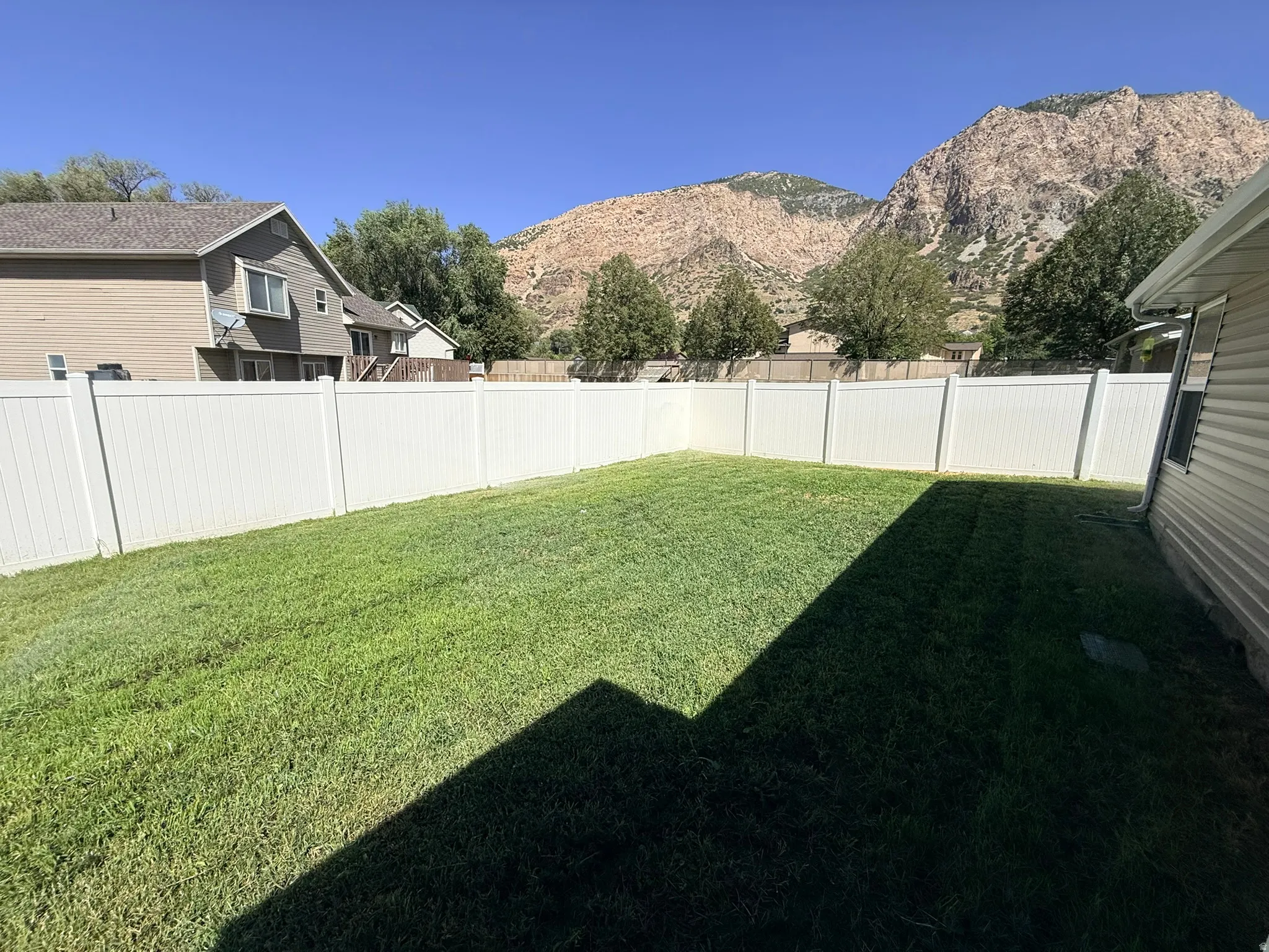 Expansive backyard featuring a green lawn, white vinyl fencing, and a mountain backdrop