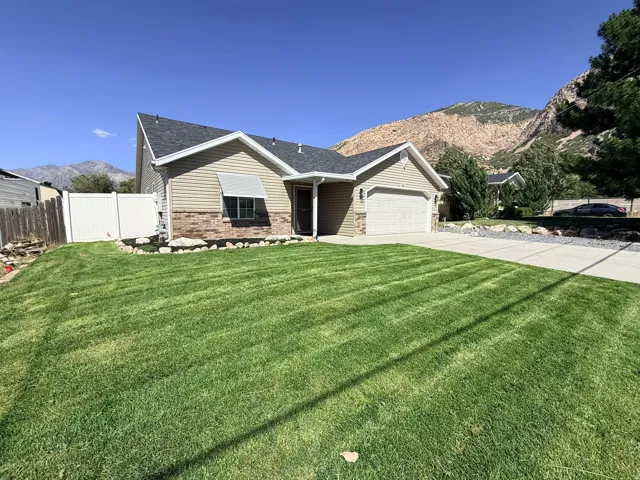 Well-maintained lawn with a paved driveway, a one-car garage, and a partial brick facade