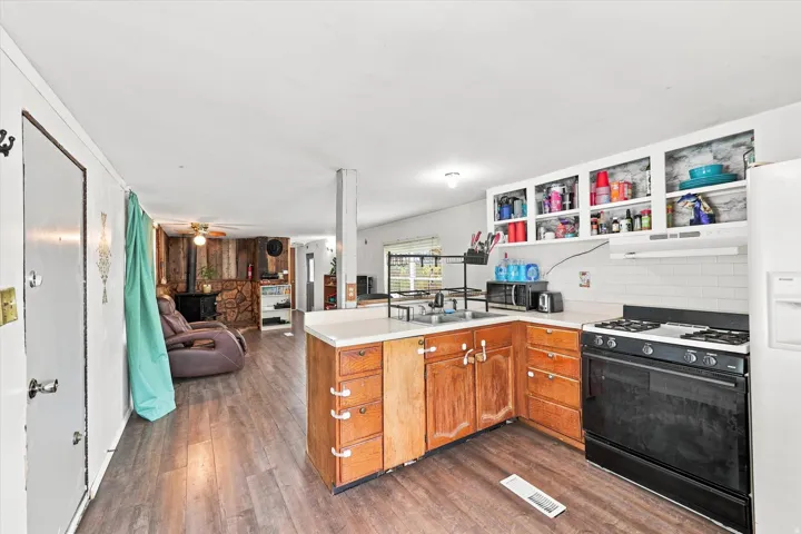 Kitchen featuring wood-finish flooring, white subway tile backsplash, gas range, open shelving, and a peninsula countertop