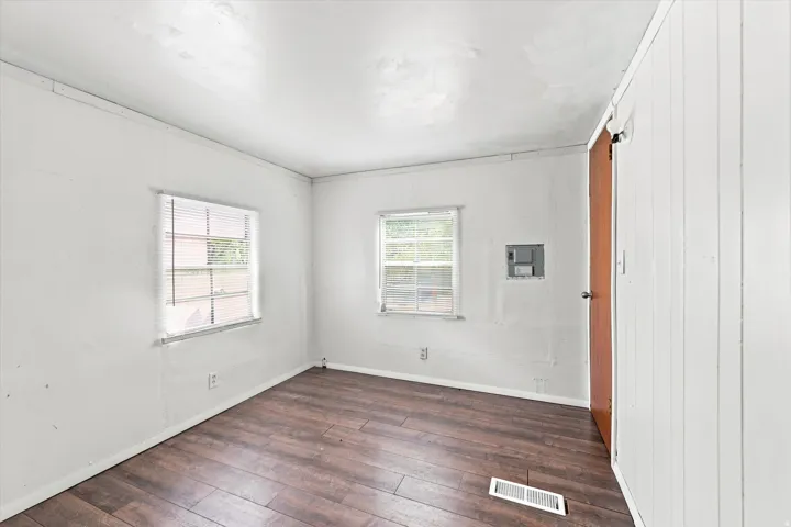 Wood-finish flooring throughout, two windows with blinds, and white vertical paneled walls
