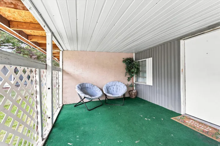 Covered front porch with a lattice railing, green floor covering, and a white entry door