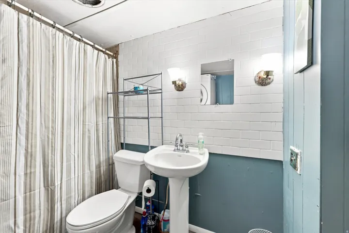 White subway tile wainscoting with a painted wall, pedestal sink with a chrome faucet, and wall-mounted light fixtures