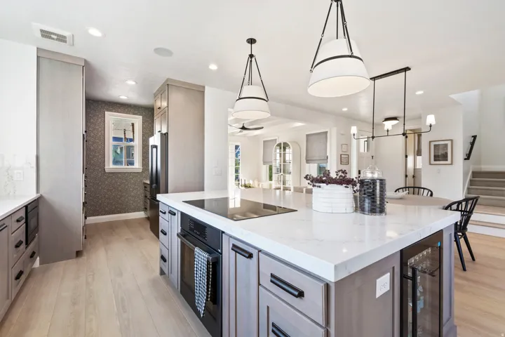 Kitchen featuring light wood-finish flooring, an expansive island with a white countertop and built-in beverage cooler, integrated cooktop, and gray cabinetry with black hardware
