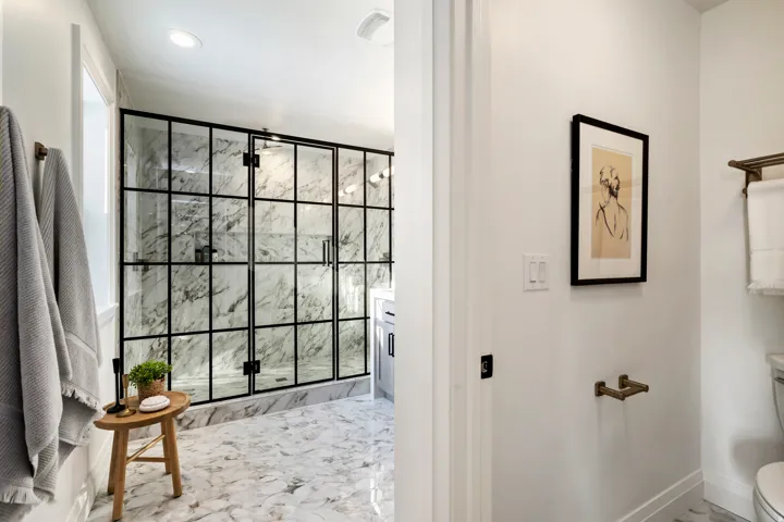 Black-framed glass shower enclosure with a white and gray veined shower surround, recessed lighting, and complementary floor tiling
