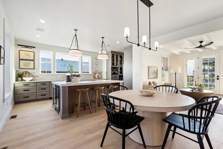 Open-concept living area with light wood-finish flooring, a kitchen island with seating, built-in wine storage, white shaker cabinets, and French doors