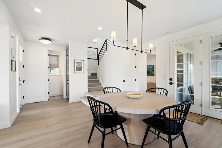 Light wood-finish flooring, recessed ceiling lighting, a modern black linear chandelier, white French doors, and a staircase with black railings