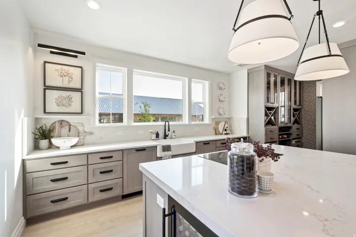 Kitchen featuring light wood-finish cabinetry, white countertops, two large pendant lights, a built-in wine storage cabinet, and a large central island