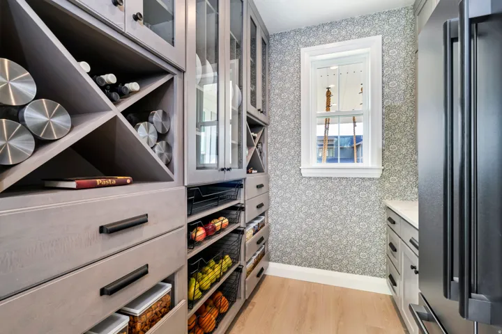 Integrated cabinetry with glass-front uppers, wine storage, and pull-out shelving, light wood-finish flooring, and a single window