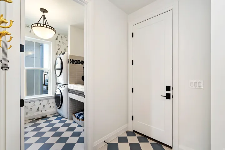 Dedicated laundry area featuring stacked appliances, a large window, and patterned floor tiling
