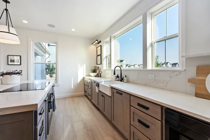 Kitchen featuring light wood-finish flooring, white countertops, a large farmhouse sink with a black faucet, light wood cabinetry with black hardware, and large windows