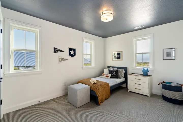 Smooth ceiling with a surface-mounted light fixture, three double-hung windows, white walls, and striped carpet flooring
