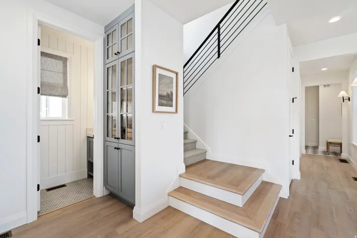 Engineered wood flooring, built-in cabinetry with glass doors, modern black metal stair railing, and a window with a fabric roman shade