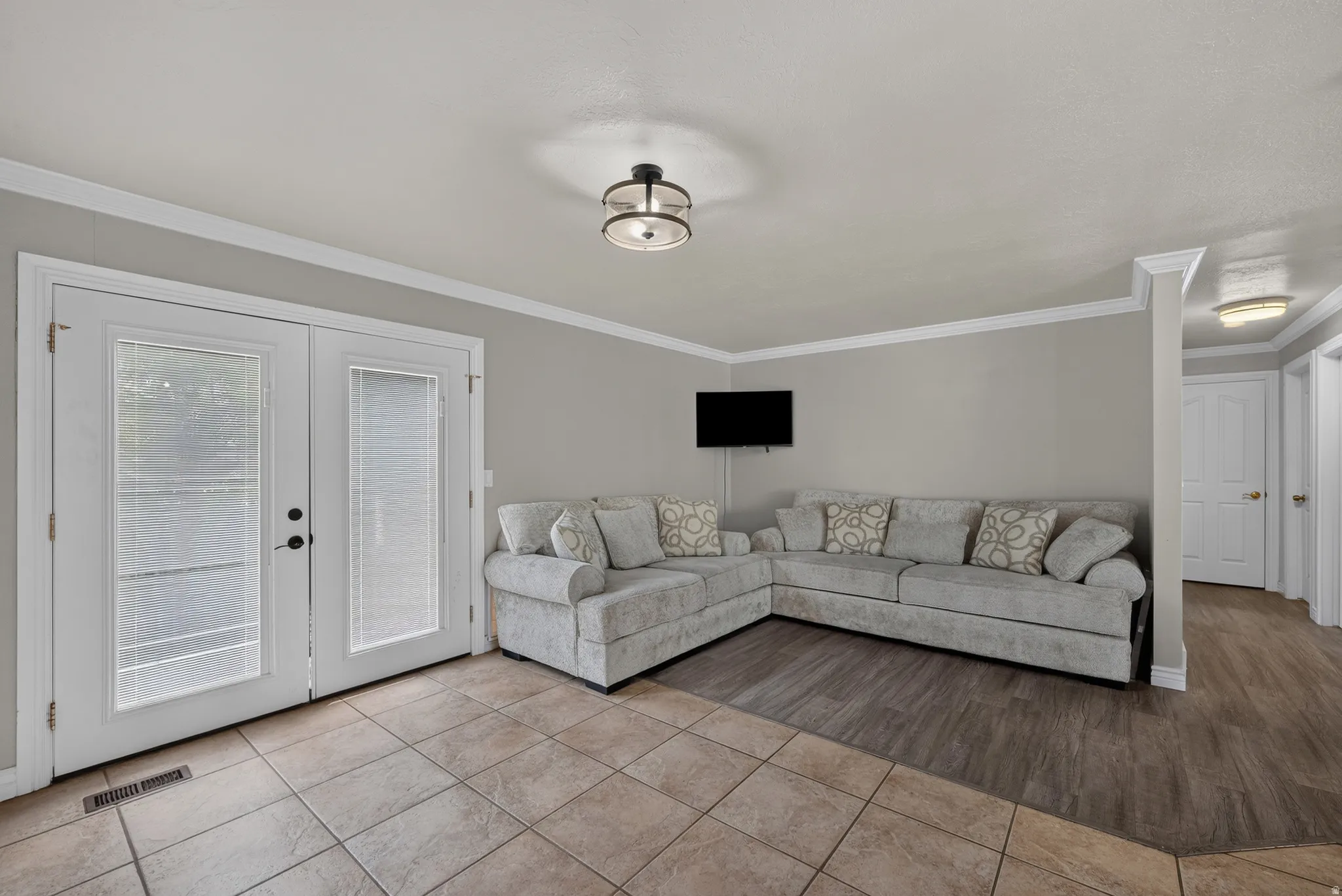 Neutral-toned walls with crown molding, double glass-paneled doors, recessed ceiling light fixtures, and multi-toned flooring