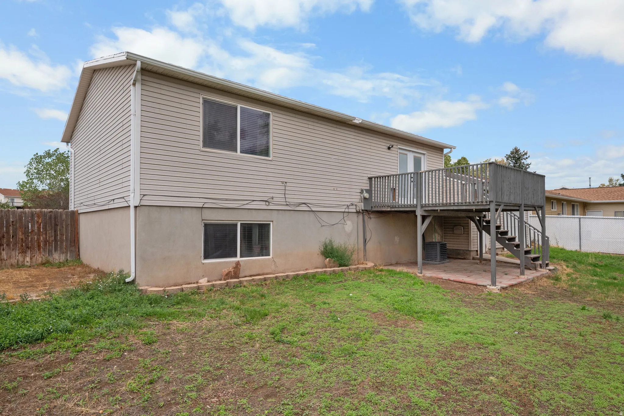 Rear exterior featuring an elevated wood deck, lower-level patio, and vinyl siding