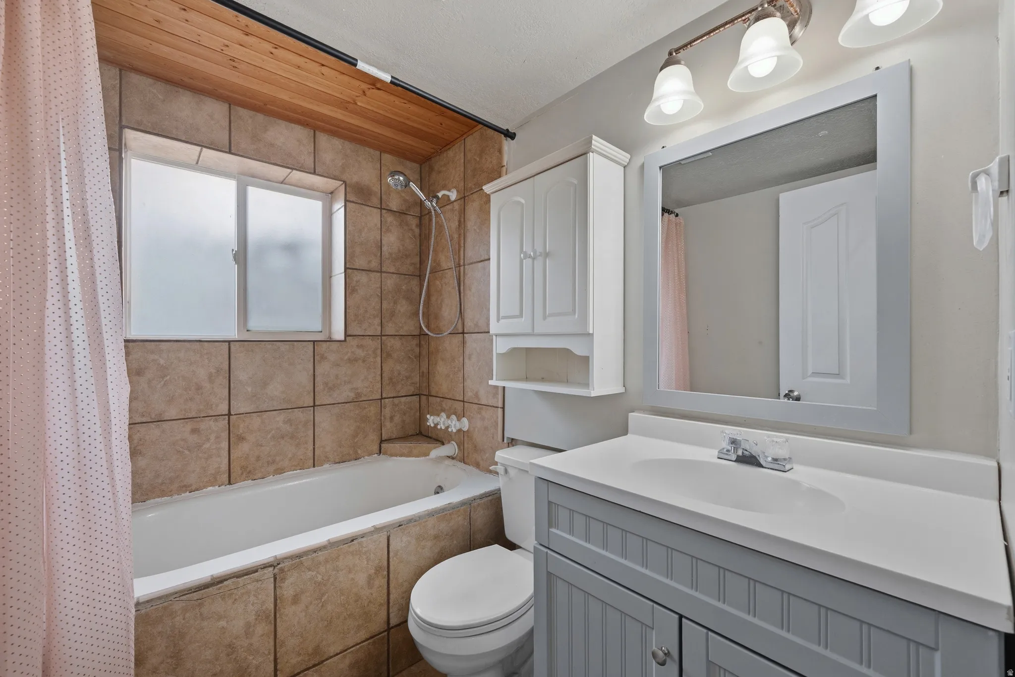 Bathroom featuring a tiled shower surround, built-in bathtub, wood-finish ceiling accent, single vanity with integrated sink, and wall-mounted storage cabinet