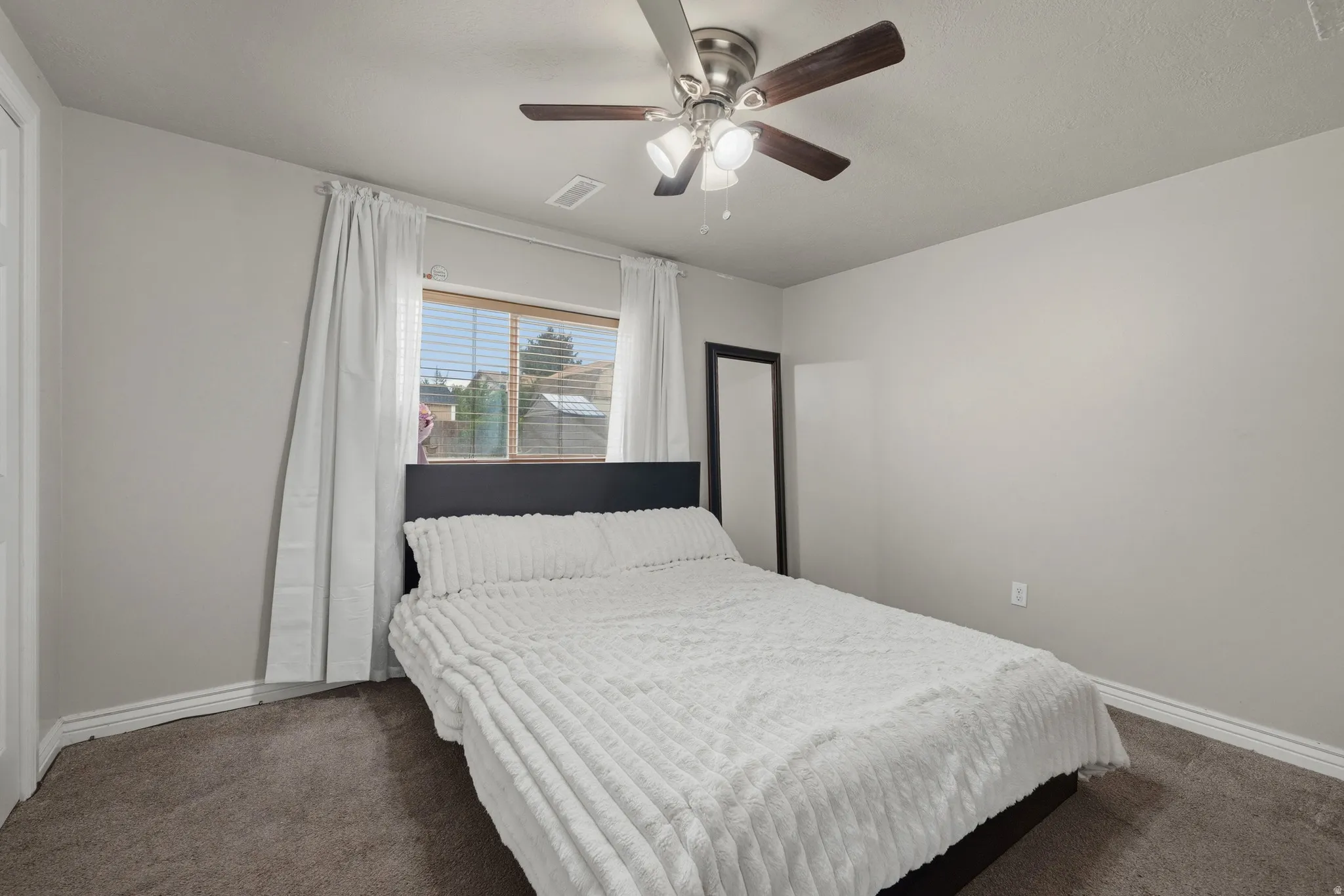 Neutral wall tones, ceiling fan with integrated lighting, carpeted flooring, and a window with blinds