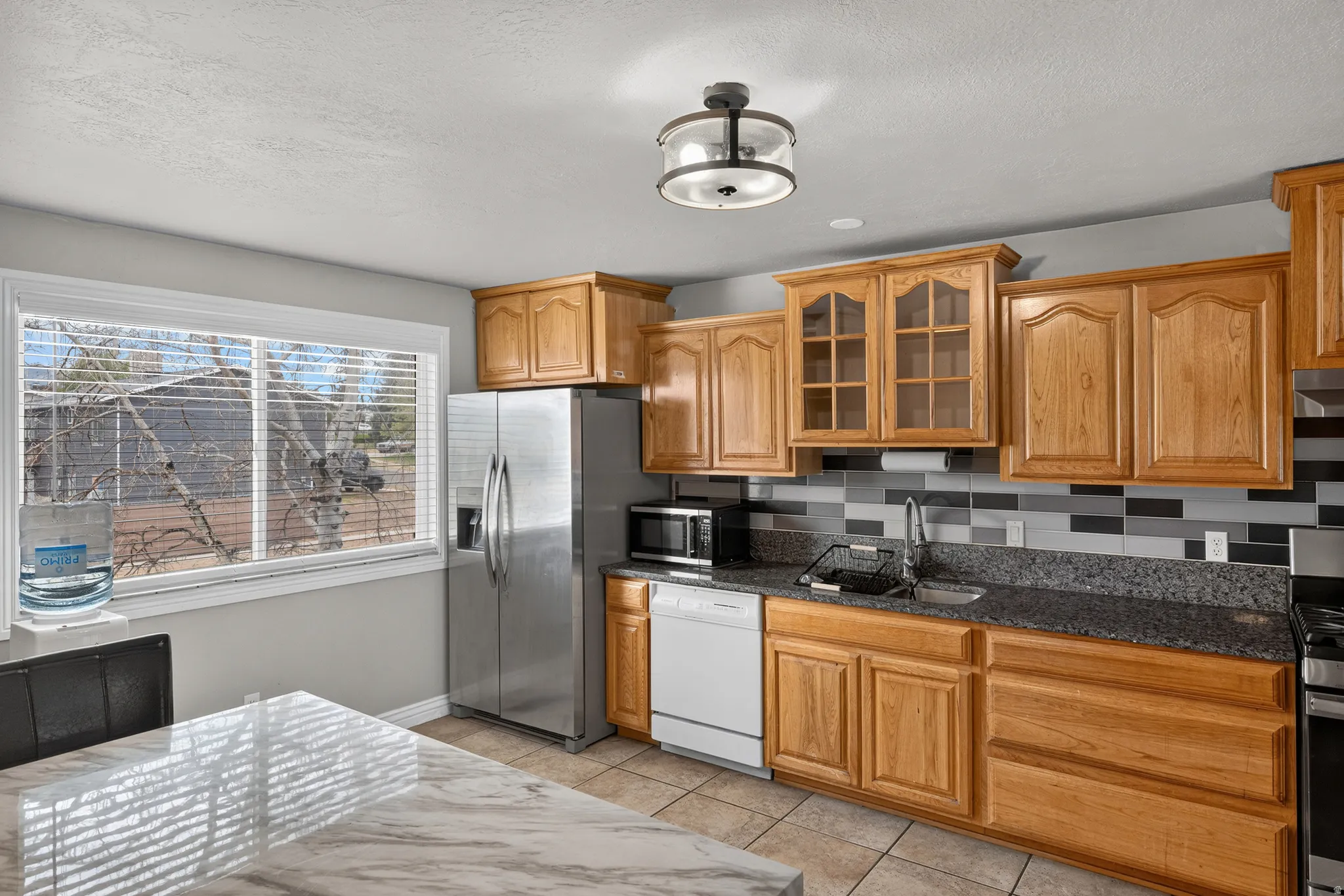 Kitchen featuring wood cabinetry, stainless steel appliances, dark speckled countertops, and a tiled backsplash