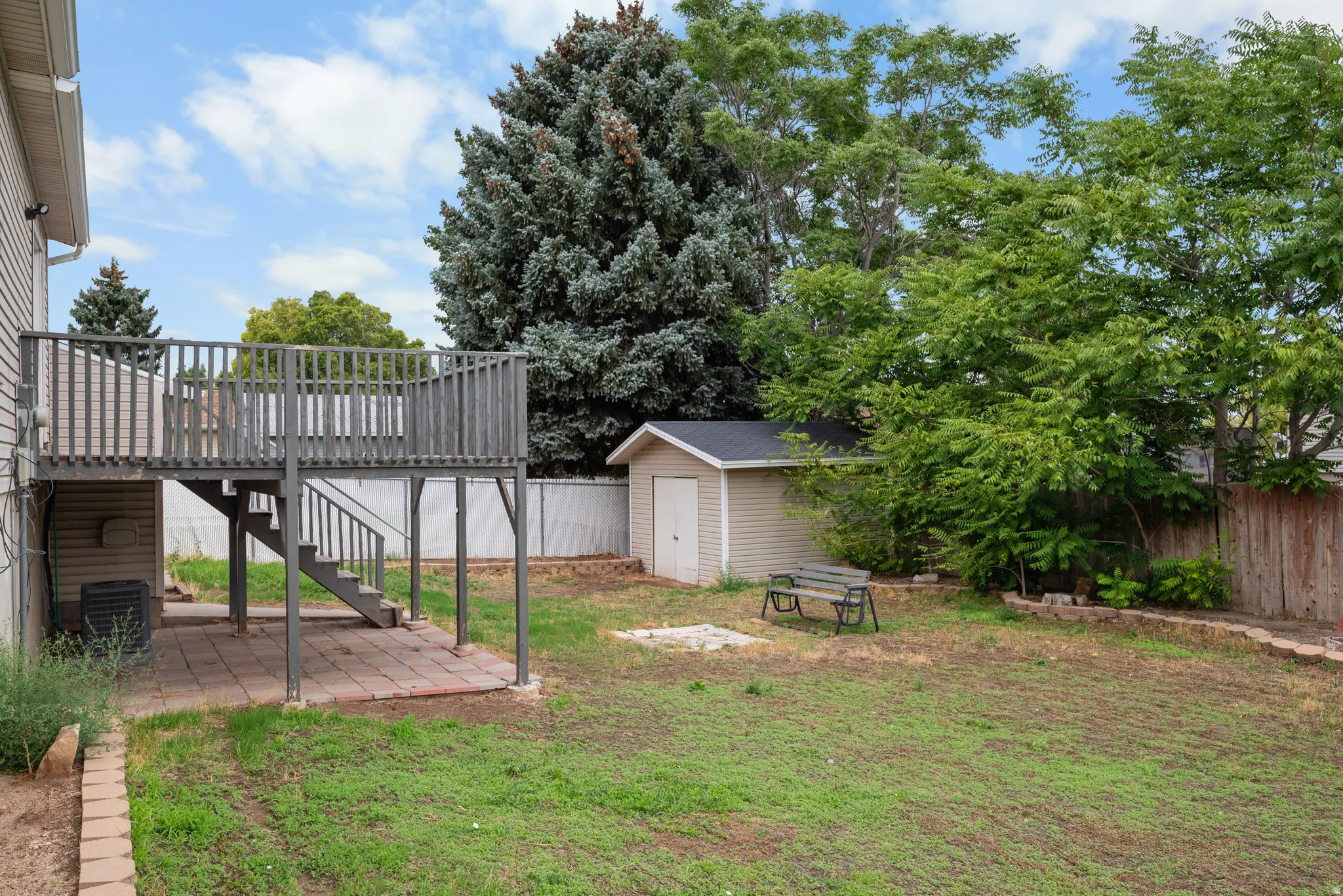 Two-story wooden deck with stairs, lower-level paver patio, detached storage shed, and a privacy fence