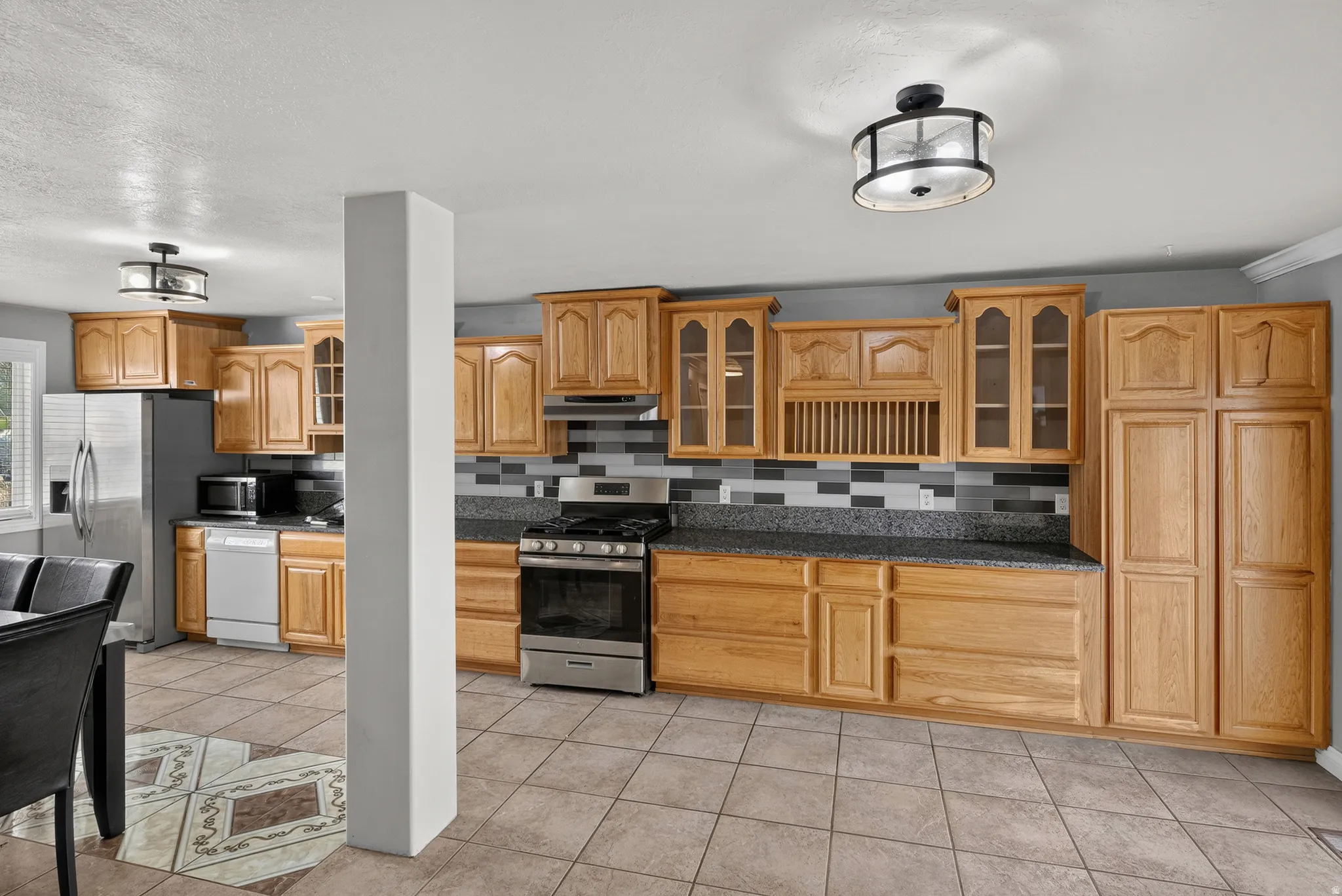 Kitchen featuring extensive wood cabinetry, stainless steel appliances, tile flooring, and a patterned tile backsplash