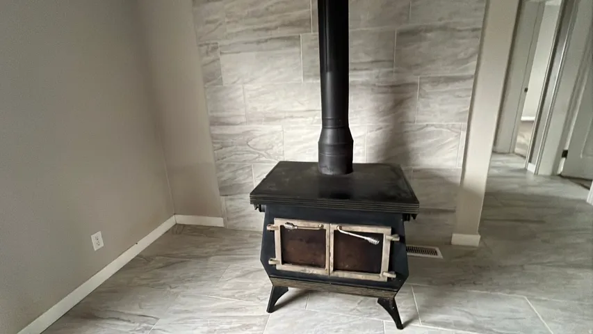 Cast iron stove with a black stovepipe, set against a tiled accent wall featuring large format rectangular tiles