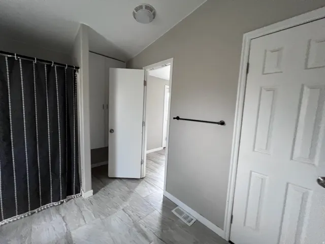 Light gray wall paint, textured ceiling, light gray large-format tile flooring, white interior doors, and a black towel bar