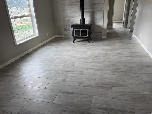 Spacious room featuring light-colored tile flooring, a wood-burning stove, and a stone-clad accent wall