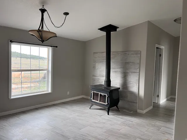 Wood-burning stove with a light-toned tile surround, large window with expansive outdoor scenery, overhead chandelier lighting, and light gray tile flooring