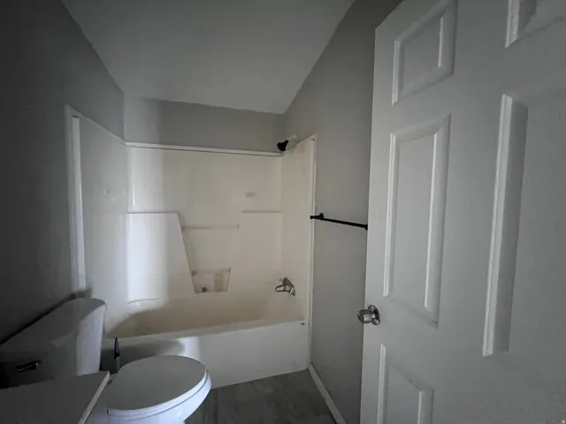 Bathroom featuring a shower-tub combination, a white toilet, and a paneled door