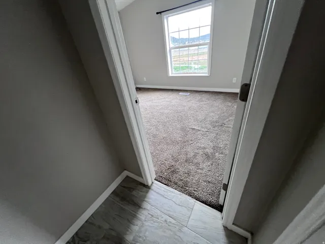 Vaulted ceiling with window, carpeted flooring, and light wall tones