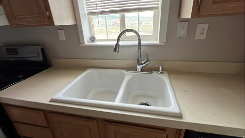 Double basin kitchen sink with a high-arc faucet, solid surface countertop, and wood-finish cabinetry