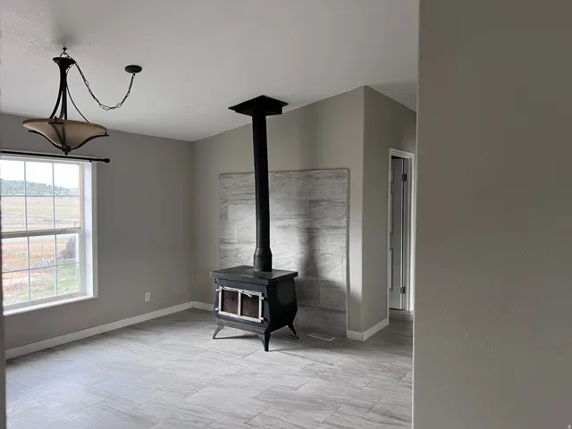 Cast iron wood-burning stove with a tiled backdrop, large window with outdoor scenery, tile flooring, and an overhead chandelier