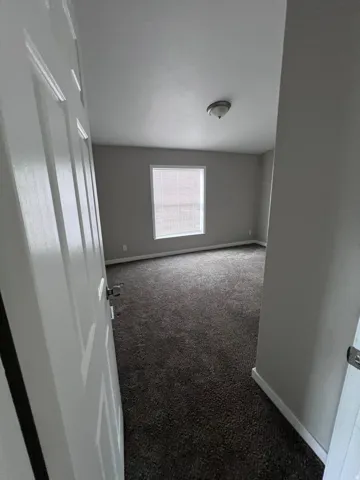 Spacious room with dark carpeting, light gray wall paint, and white trim