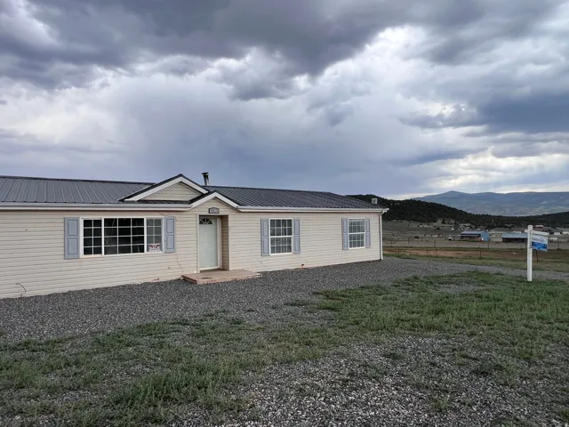 Residence featuring light-colored siding, multiple windows with shutters, and a grey metal roof