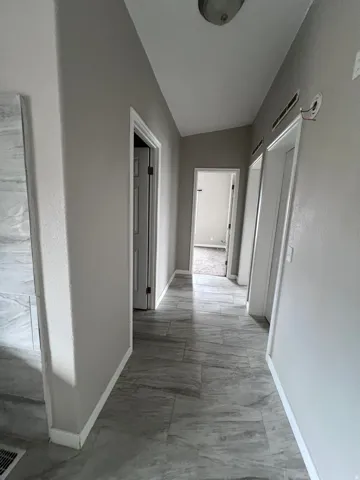 Hallway featuring gray-toned tile flooring, light-colored walls, white trim, and overhead lighting