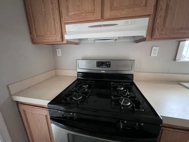Wood-finish cabinetry, light-toned countertops, and a stainless steel and black range
