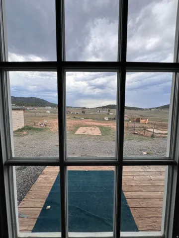 Window with multiple panes, revealing a wood-plank deck, gravel ground covering, and distant hills