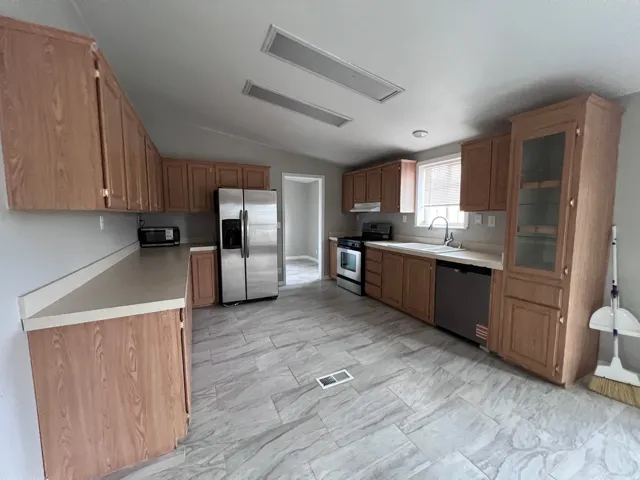 Kitchen featuring wood-finish cabinetry, stainless steel appliances, light-toned countertops, and large format floor tiling