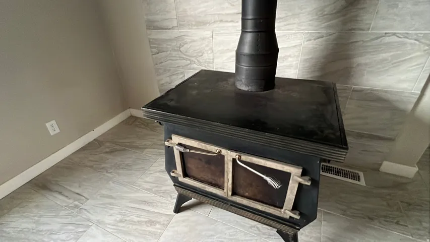 Cast iron wood-burning stove with a black stovepipe, set against a tiled wall and tiled flooring