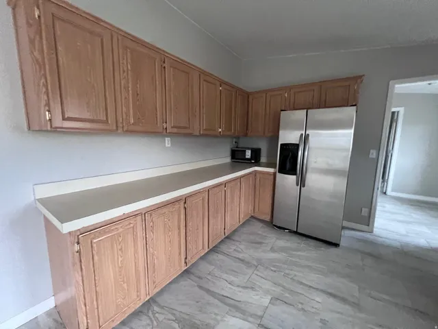 Kitchen featuring wood-finish cabinetry, light-toned countertops, and a stainless steel refrigerator