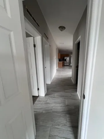 Hallway with gray tile flooring, white paneled doors, light gray wall paint, and a ceiling-mounted light fixture