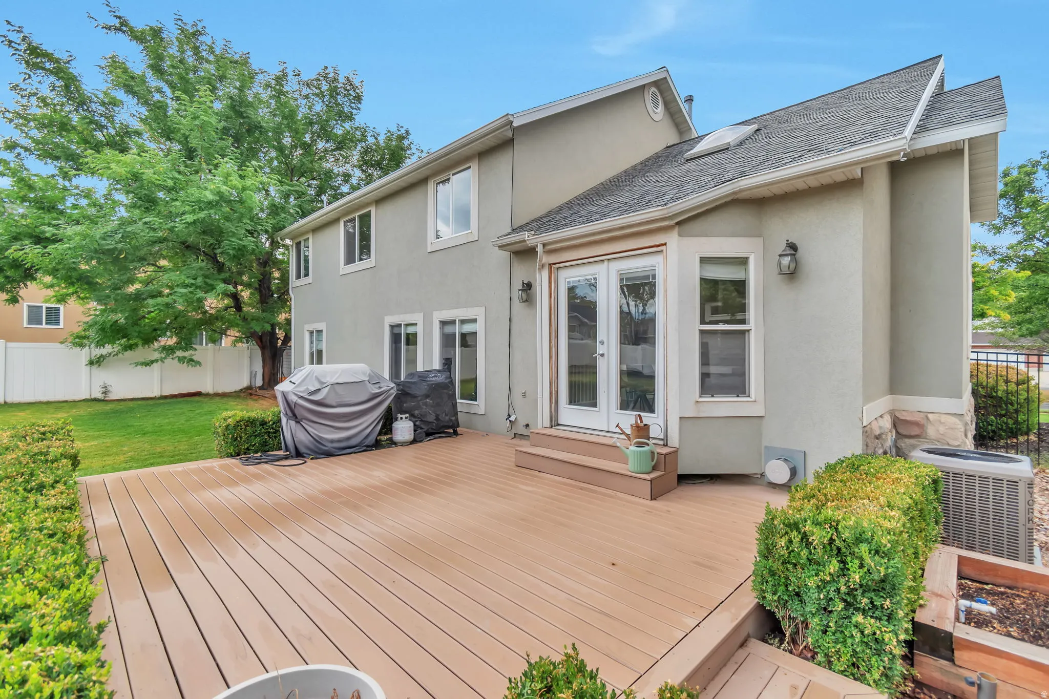 Expansive wood-finish deck with integrated steps, stucco exterior, multiple windows, and dual paneled glass doors